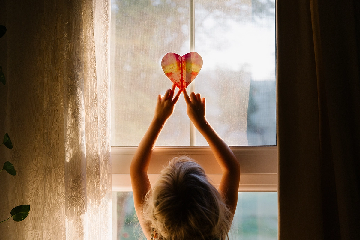 Child placing a love heart on a window